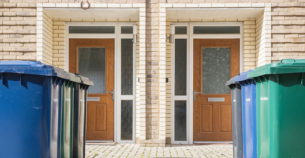 England council recycling rates represented by waste bins lined up outside two front doors.